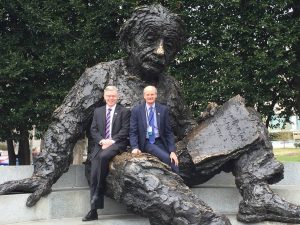 Two men in suits sitting on the leg of a large statue of Albert Einstein.