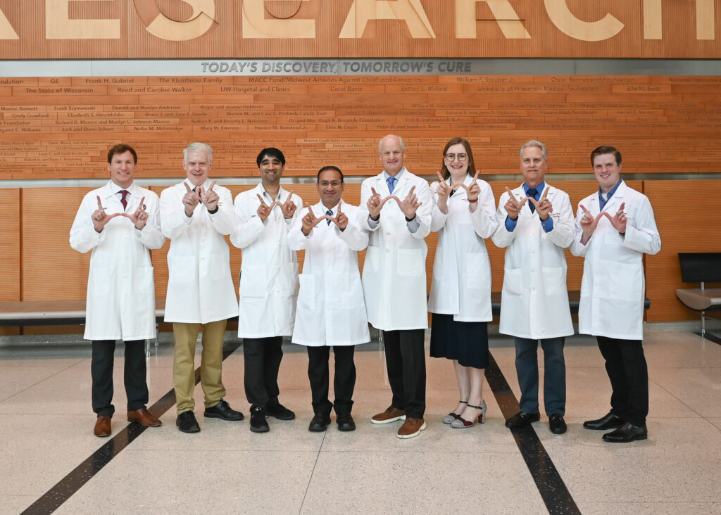 Eight people stand in a row, holding their hands in a 'w' for Wisconsin.