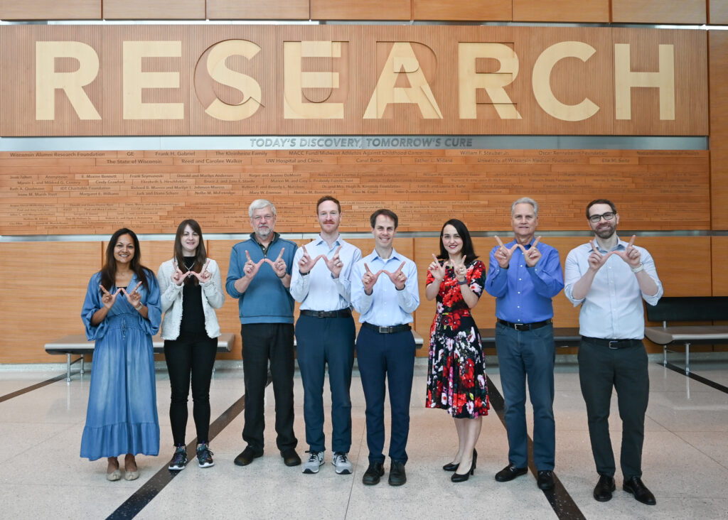 Eight people stand in a line with their hands in a 'w' for Wisconsin.